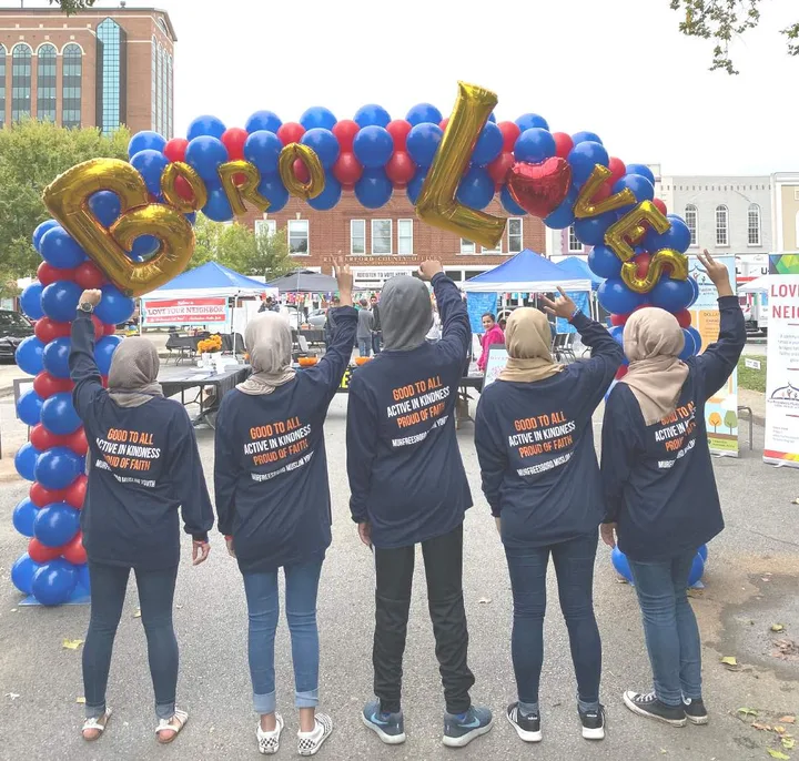 MMY volunteers with arms raised under a "Boro Loves" balloon arch at Love Your Neighbor