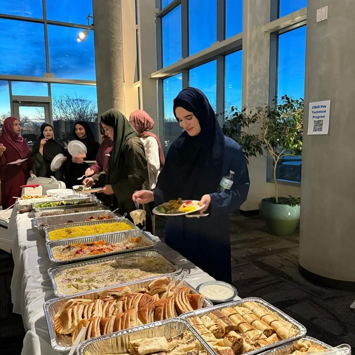 A volunteer serving food from trays at an MMY iftar